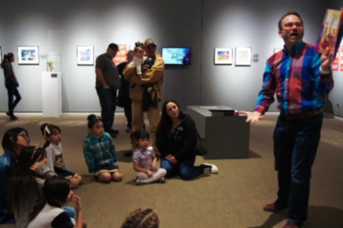 Male Brownsville intern reads to preschoolers in a museum.